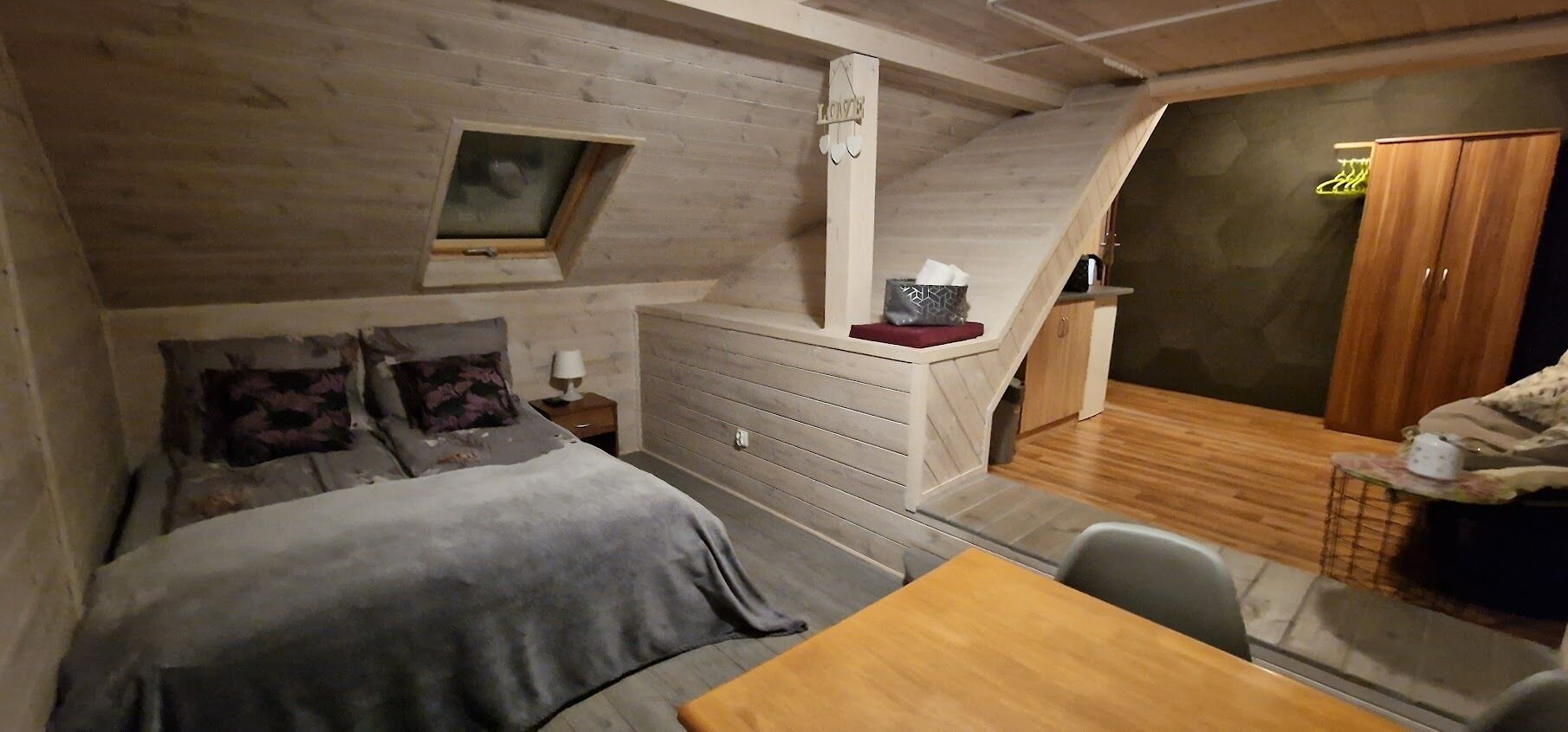A cozy room with a bed, a small table, a wooden cabinet, and a window.