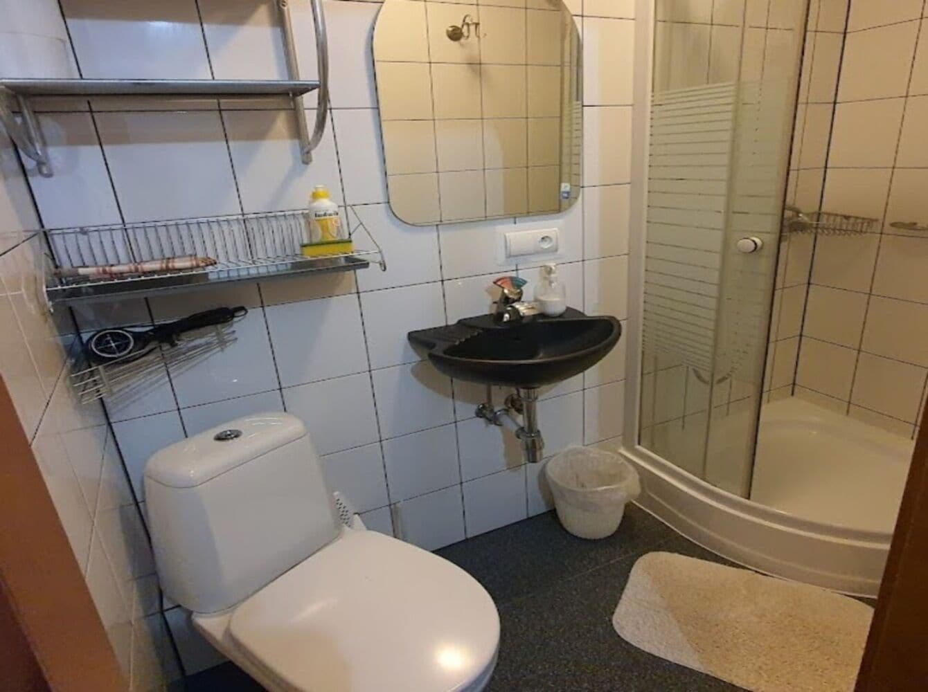 Un baño con inodoro, lavamanos, espejo, ducha y paredes con azulejos.