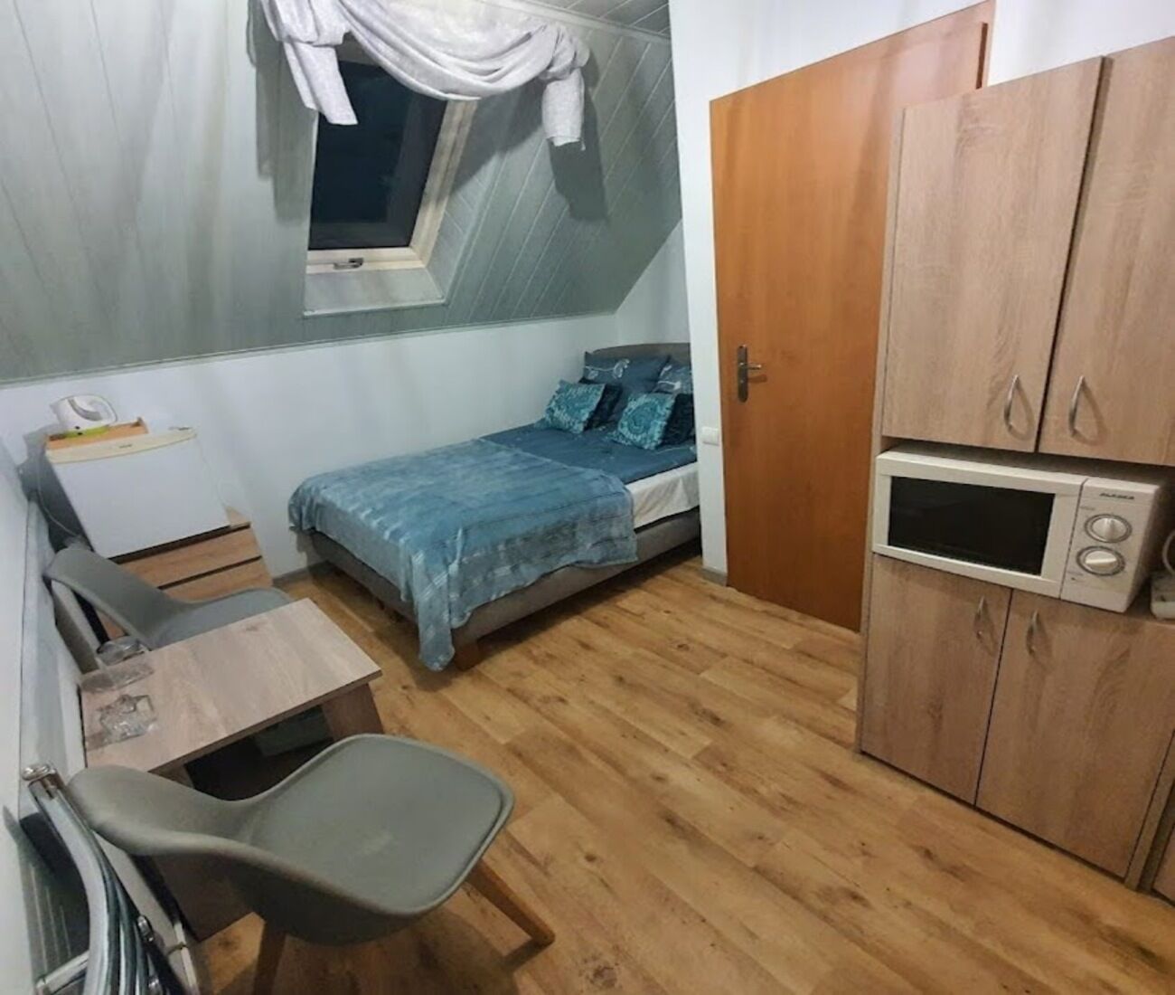 A small bedroom with a bed, a desk, a chair, a wardrobe, and a microwave.