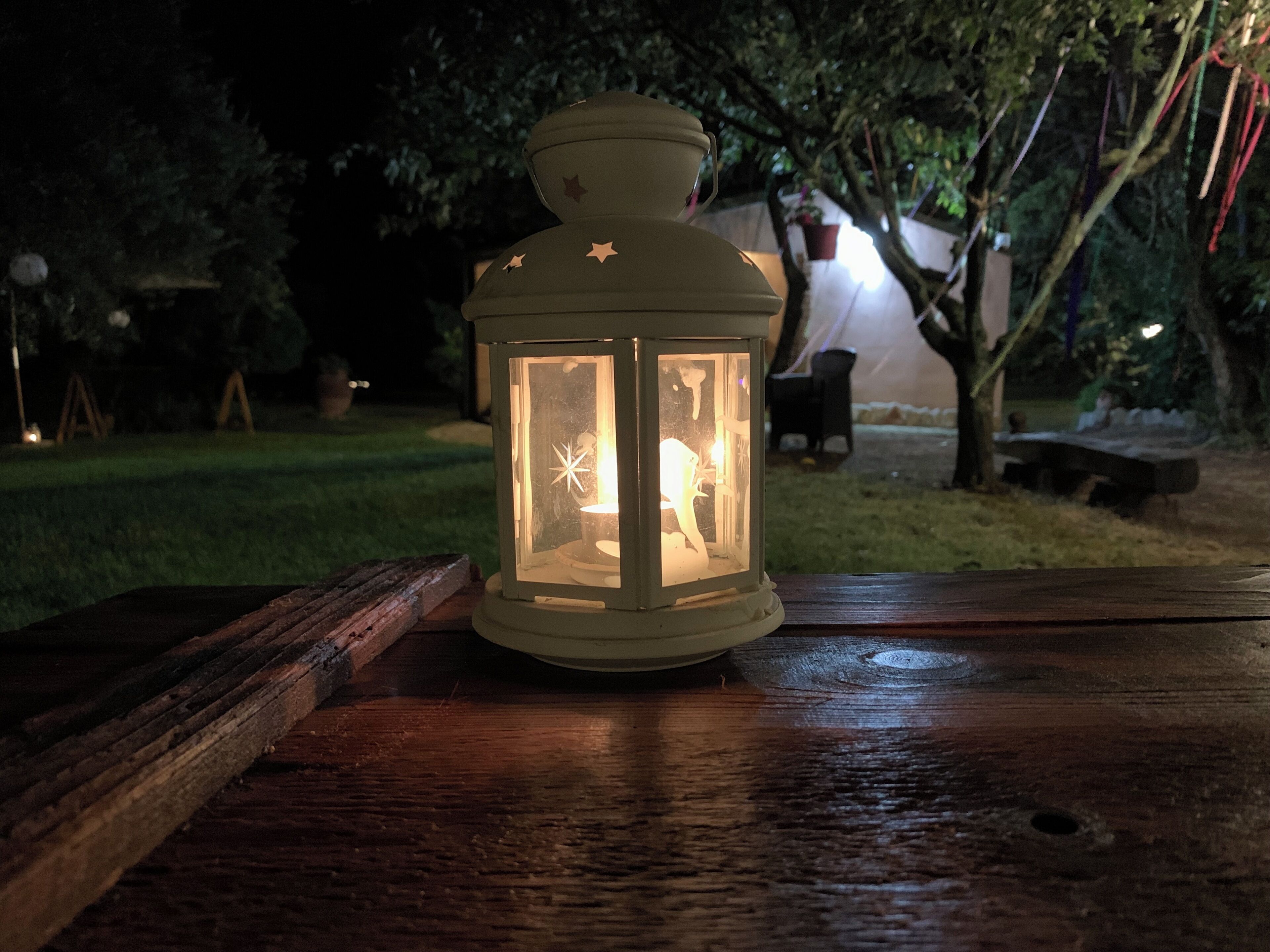 Eine Laterne auf einer Holzfläche im Freien bei Nacht.