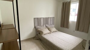 Ein Schlafzimmer mit einem Bett, einem Kopfteil, einem Fenster mit Vorhängen und einer Holzregaleinrichtung.