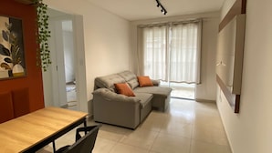 Ein modernes Wohnzimmer mit grauem Sofa, orangefarbenen Kissen, einem Holzessttisch und einem schwarzen Sessel.