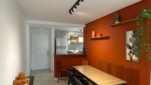 Ein moderner Essbereich mit einem Holztisch und schwarzen Stühlen, im Hintergrund eine Küche und dekorative Regale mit Pflanzen.