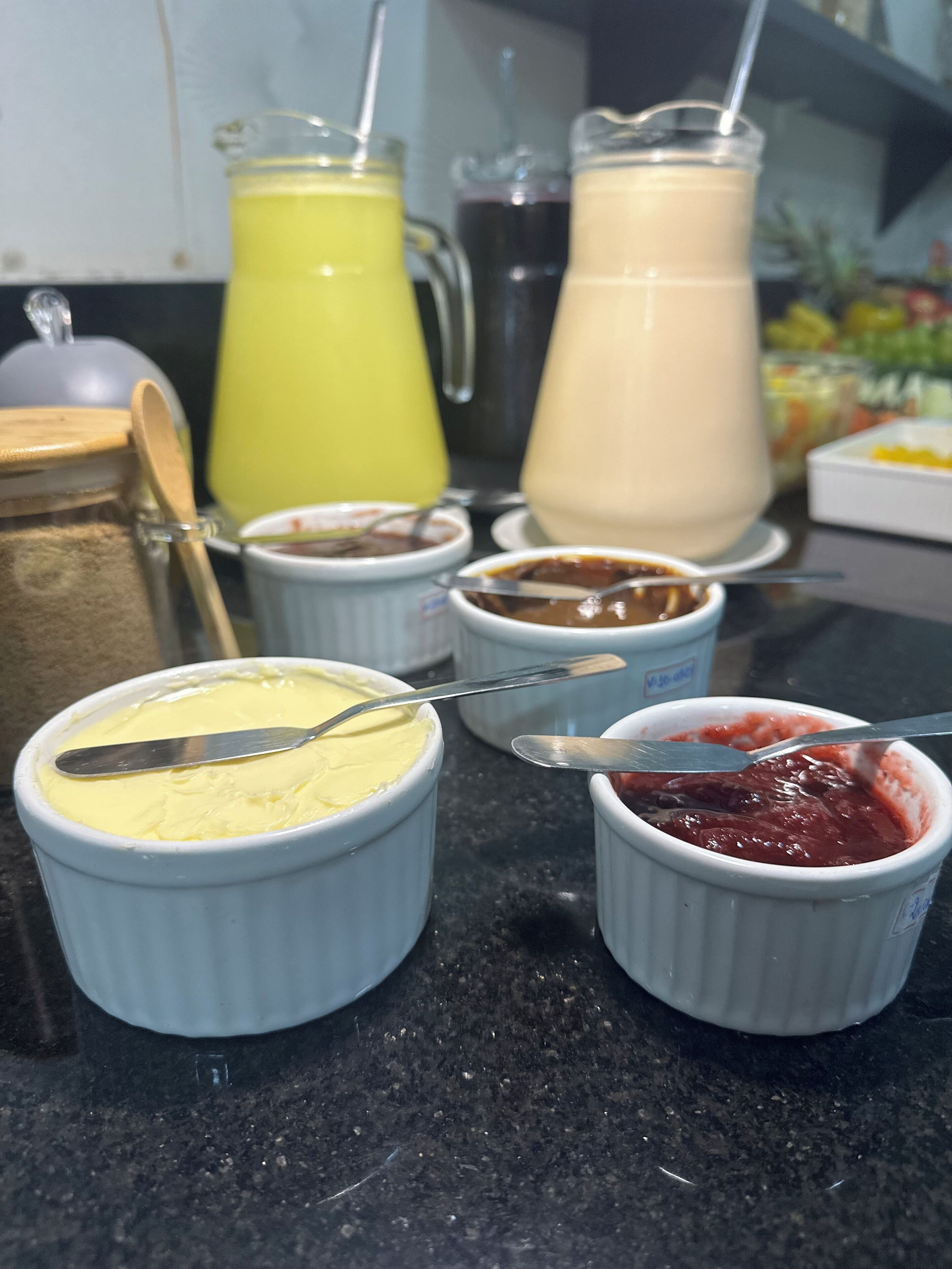 Una encimera de cocina con diversos alimentos y bebidas, incluyendo una jarra de líquido amarillo, una jarra de líquido blanco y varios recipientes pequeños con diferentes salsas.