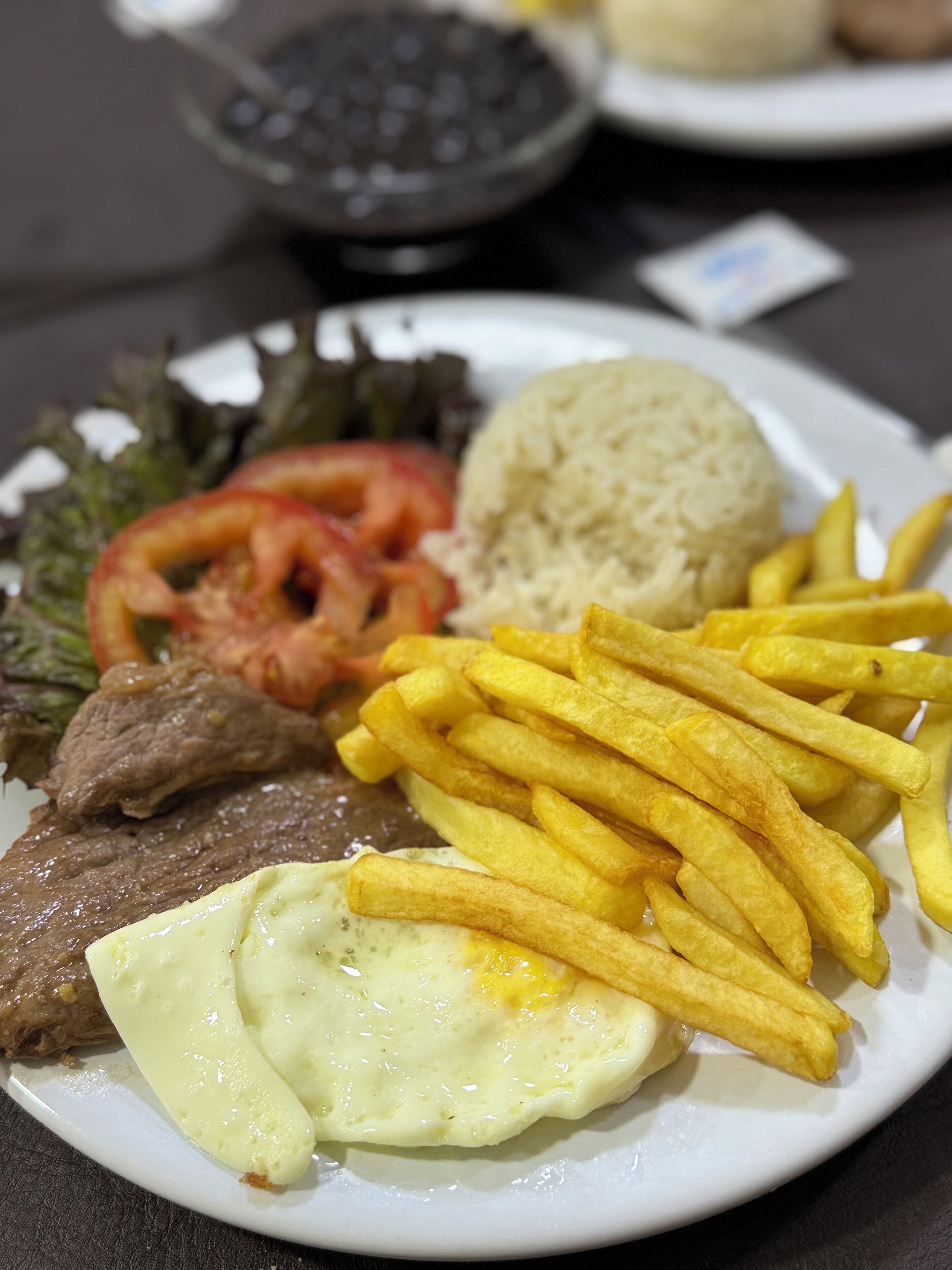 A plate of food including steak, eggs, fries, rice, and vegetables.