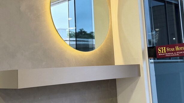 A modern hotel interior with a large circular mirror on a wall, a sign for the SH Star Hotel, and a clean, minimalist design. - STAR HOTEL (Chapecó)