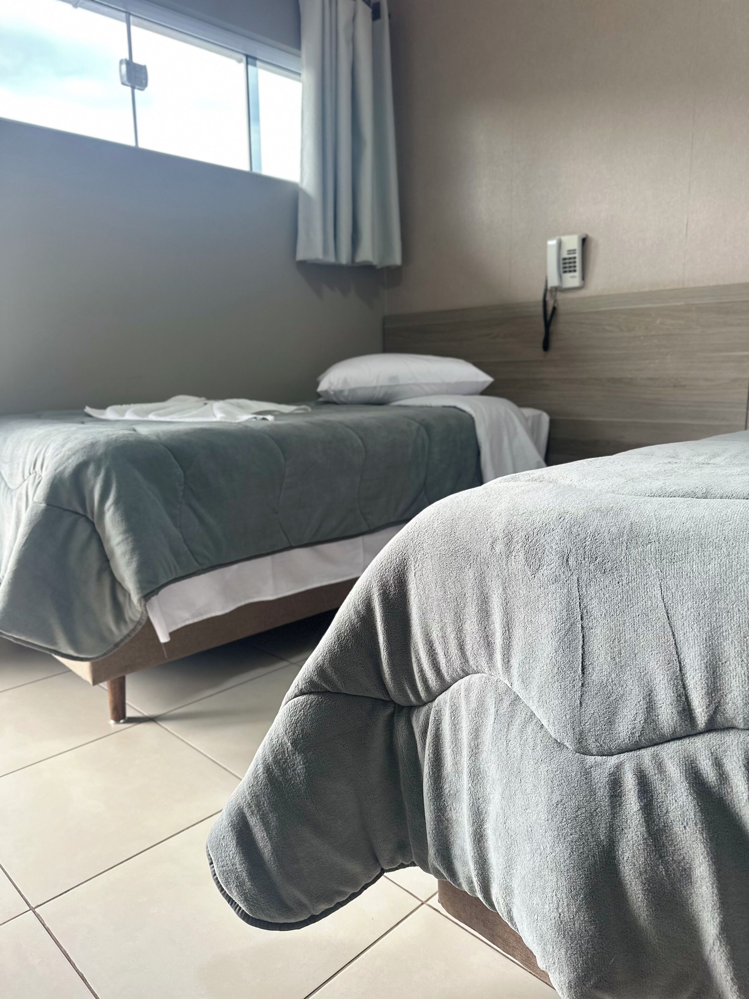 Duas camas de casal com roupa de cama cinza em um quarto de hotel.