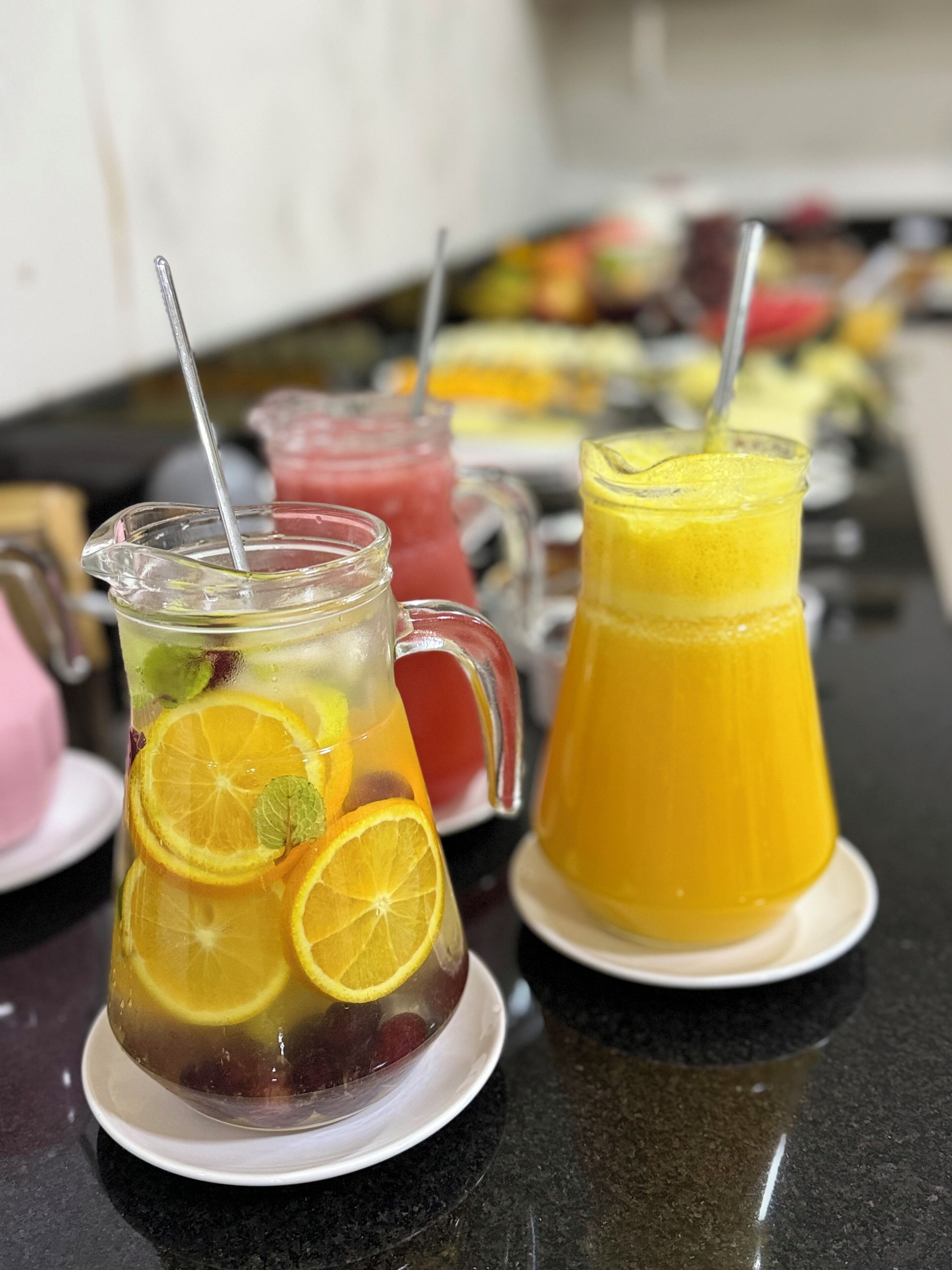 Une table sur laquelle se trouvent diverses boissons, notamment un pichet contenant des tranches d’orange et de la menthe, un autre pichet avec une boisson jaune et un verre contenant une boisson rouge.