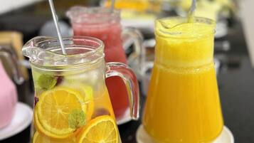 Une table sur laquelle se trouvent diverses boissons, notamment un pichet contenant des tranches d’orange et de la menthe, un autre pichet avec une boisson jaune et un verre contenant une boisson rouge.