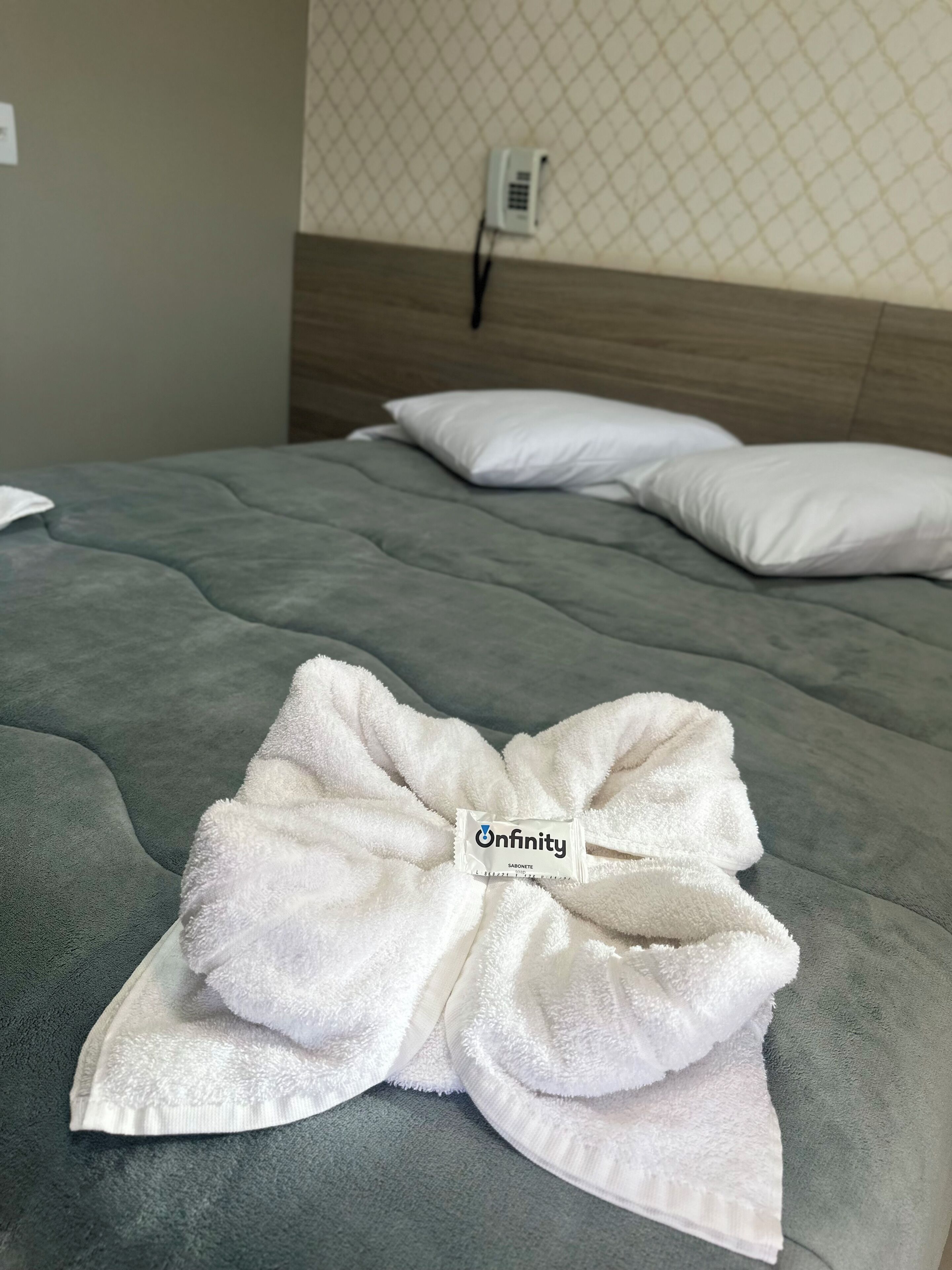 A neatly made bed with a white towel arranged in a bow shape on the bedspread.