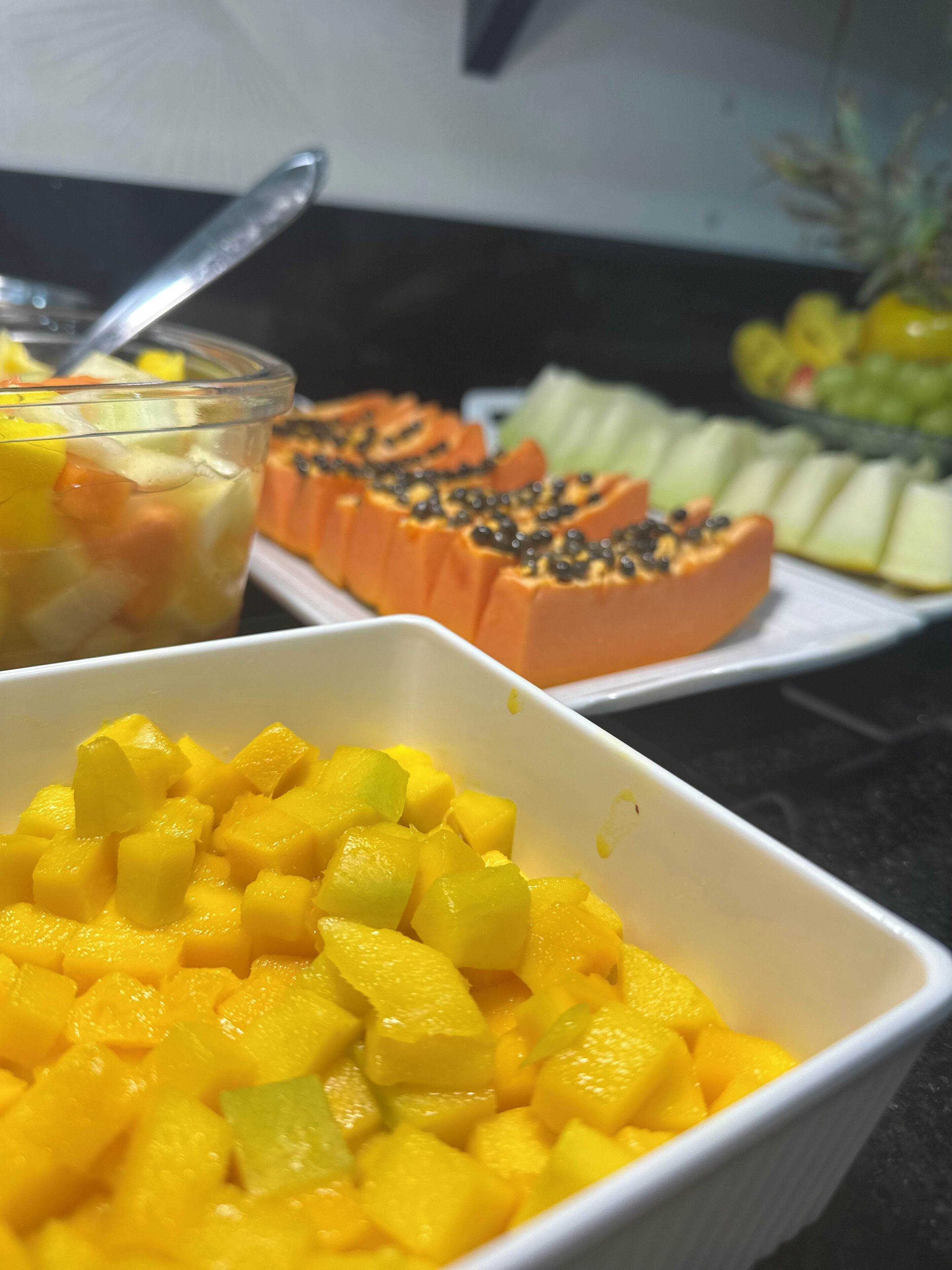 A buffet with various fruit dishes, including diced mango, papaya, and melon.