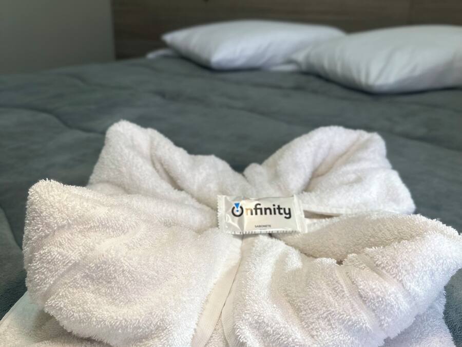 Toalha branca dobrada, com etiqueta, sobre uma cama em quarto de hotel.