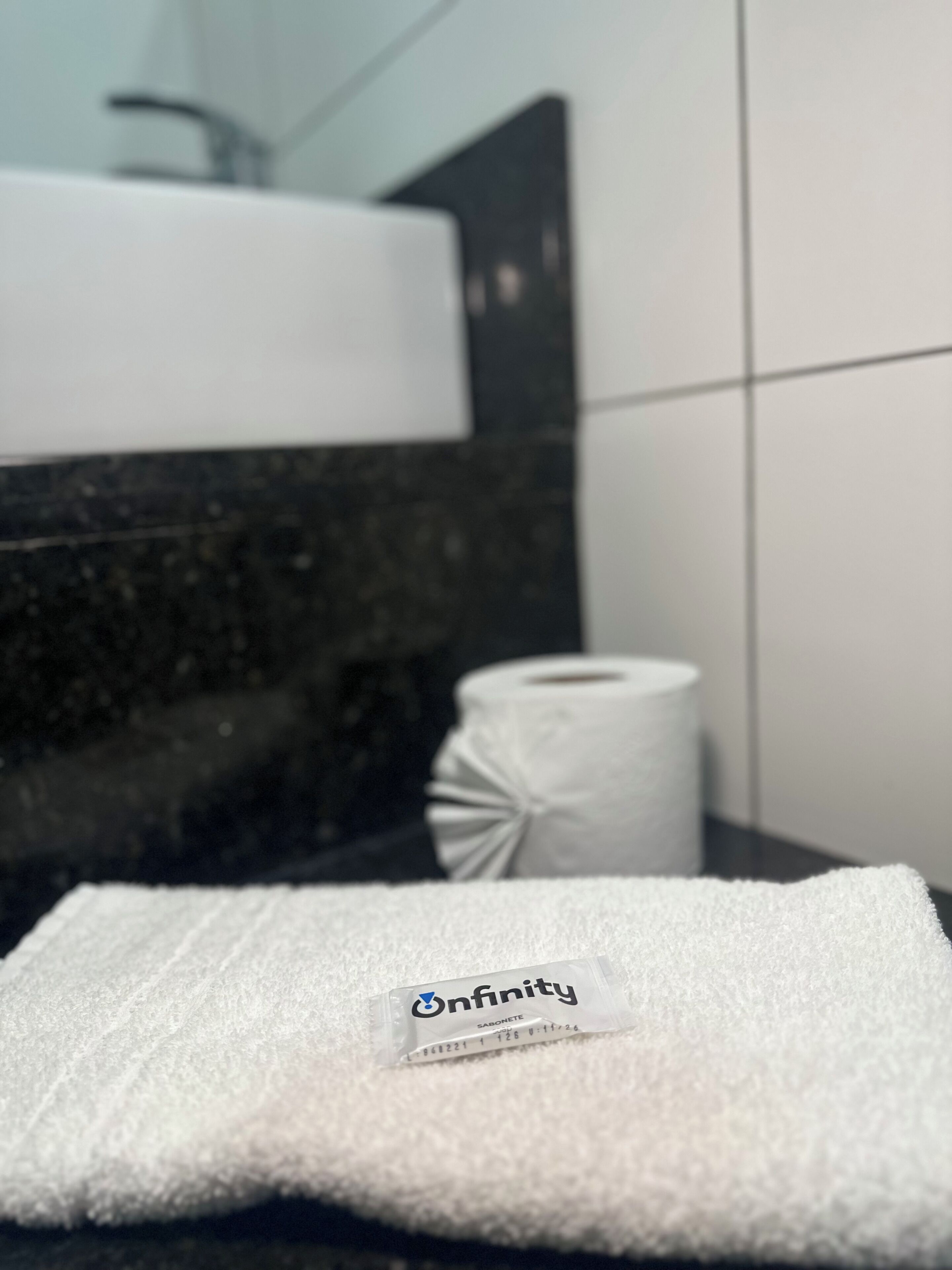 A bathroom with a white towel labeled 'Infinity' and a toilet paper roll on a dark countertop.