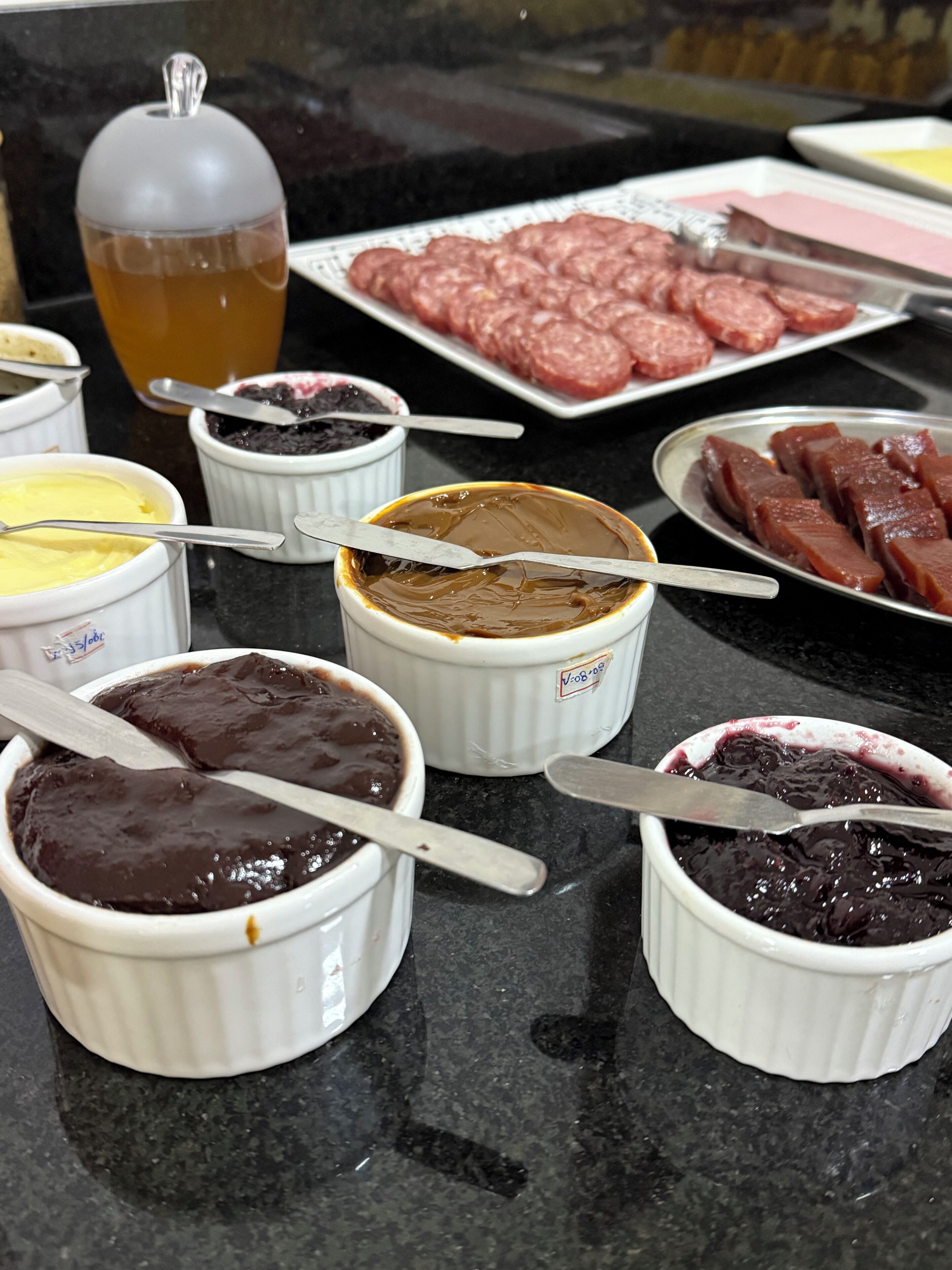A table with various food items including bowls of chocolate and jam, a plate of sliced meat, and a glass of iced tea.