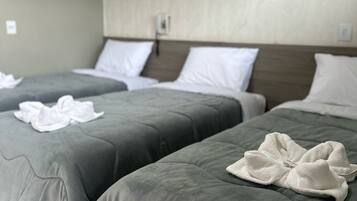 Twee bedden met grijze lakens en witte handdoeken, een wandairconditioner en een effen muur met een lichtschakelaar.