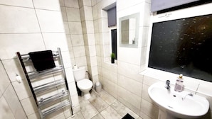 Une salle de bain équipée de toilettes, d’un lavabo, d’un porte-serviettes et d’une petite plante en pot.