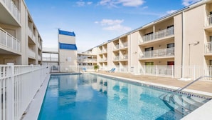 A swimming pool surrounded by multi-story buildings with balconies, a clear sky, and a lifeguard chair. - Sugar Beach 345e (Orange Beach)