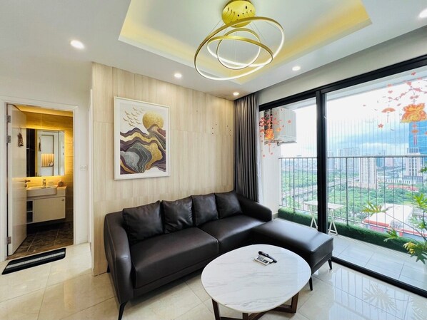 A modern living room with a black leather sofa, a round coffee table, and a large window offering a city view.