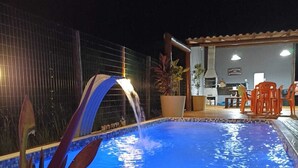 A swimming pool with a water feature, surrounded by a fence, potted plants, and outdoor seating. - FLAT SHELDOM (Maraú)