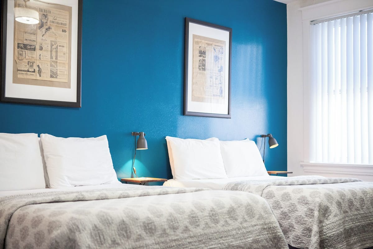 A hotel room with two beds, a blue wall, and framed pictures on the wall.