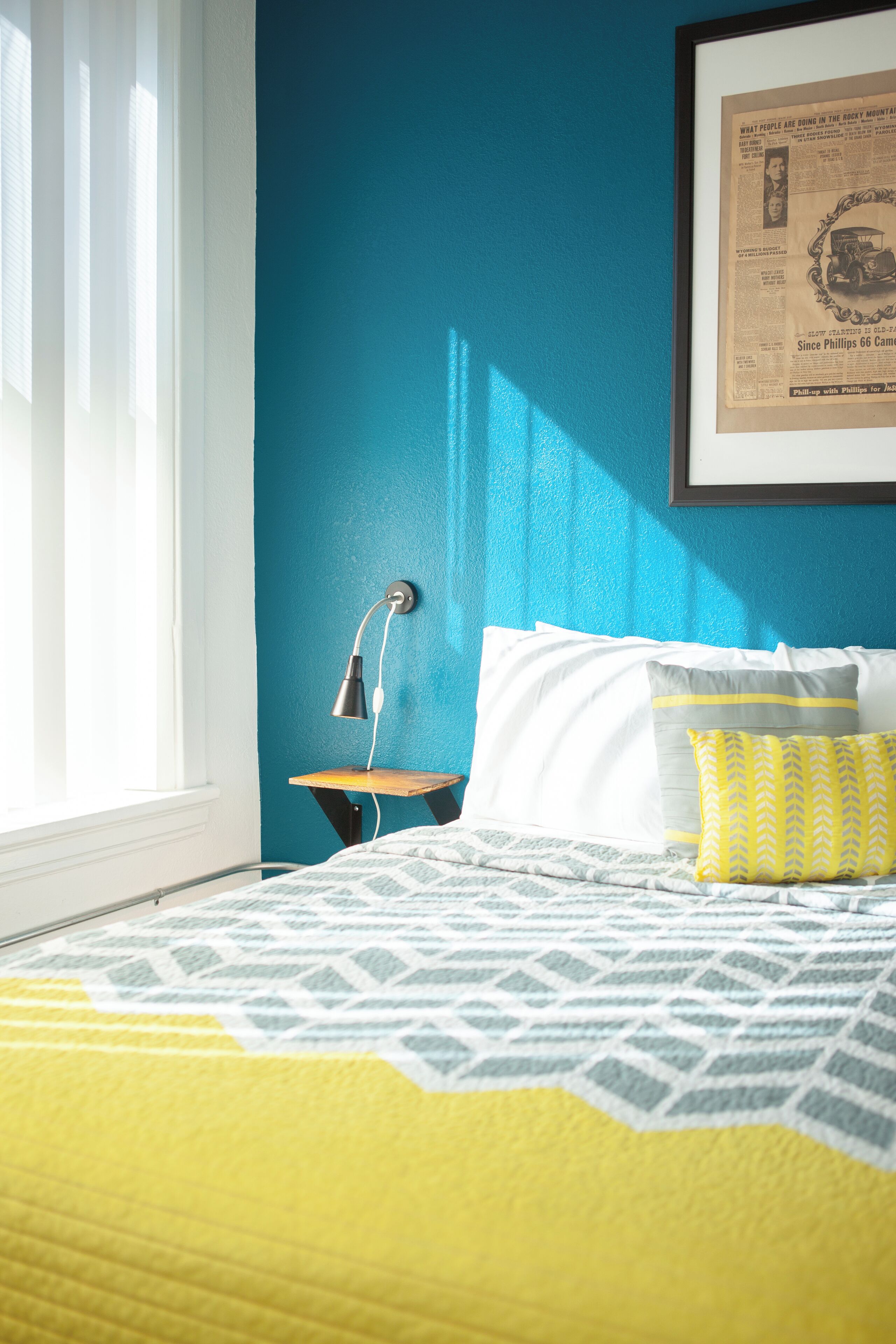 A neatly made bed with a patterned bedspread, a bedside lamp, and pillows against a blue wall.