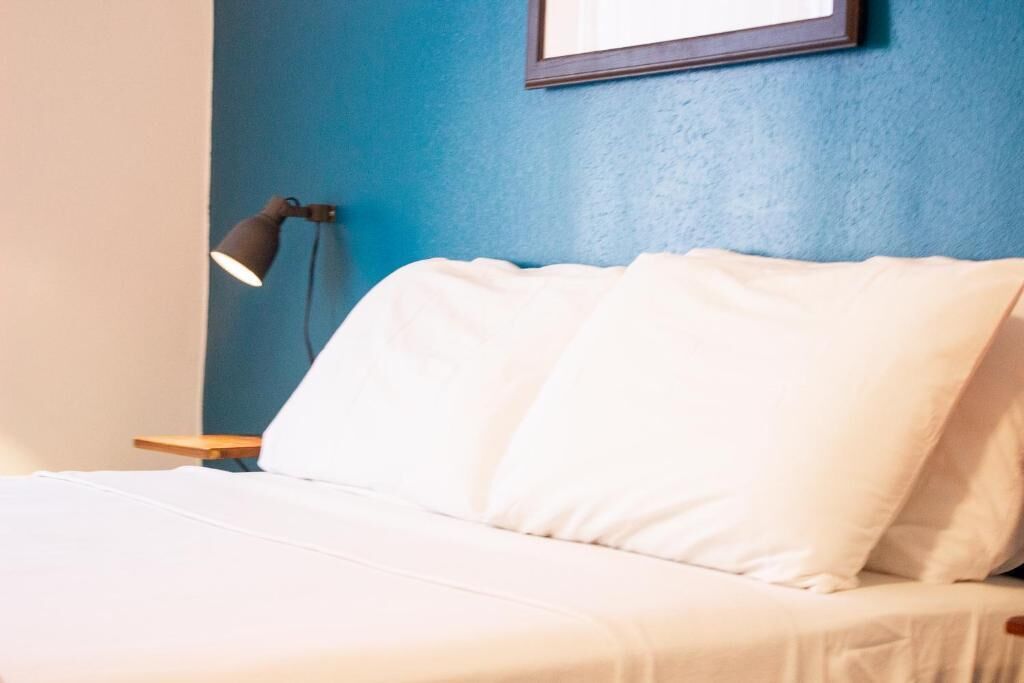 Een bed met witte lakens in een kamer met een blauwe muur en een lijst met een afbeelding erboven.
