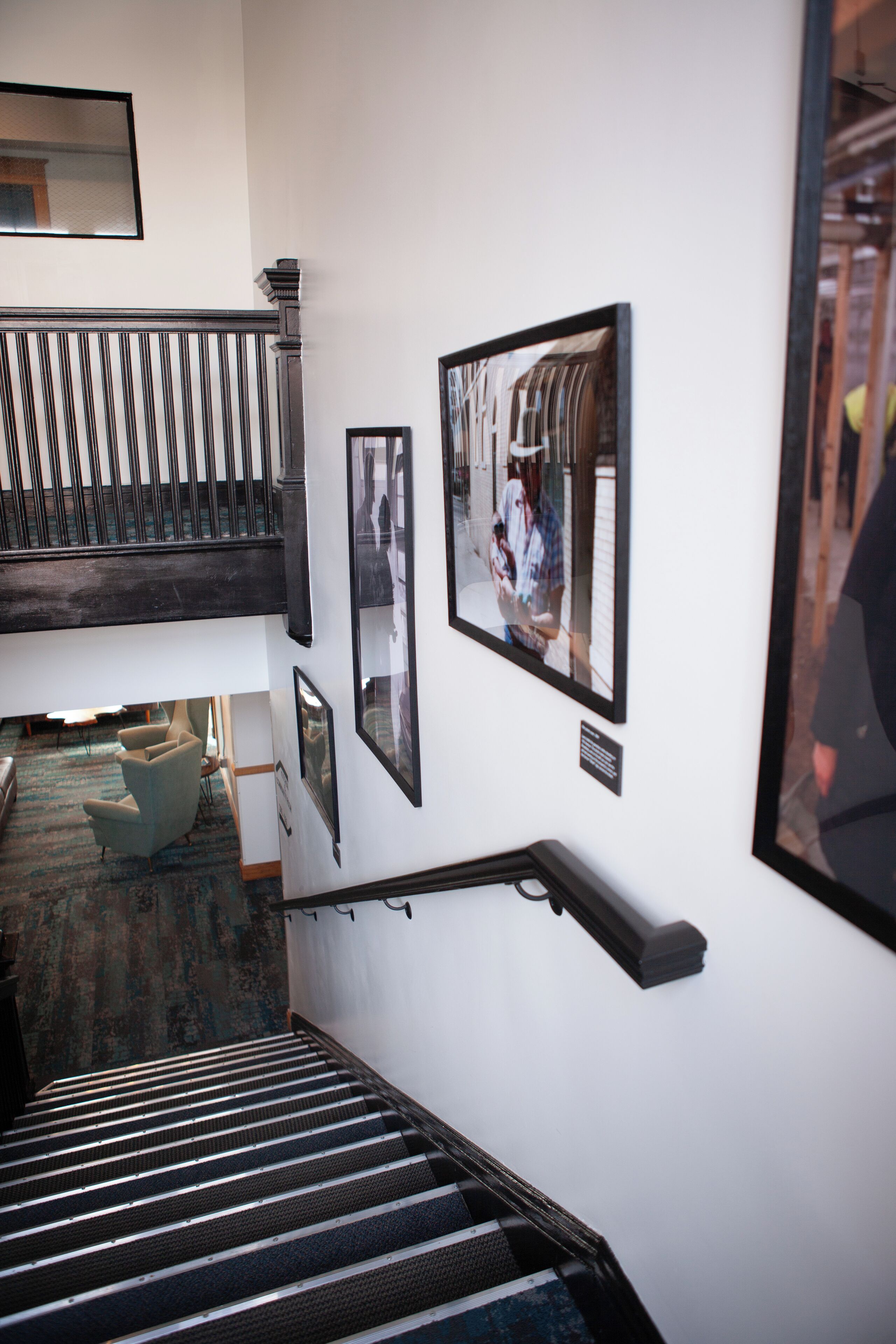 A staircase with a handrail, a wall with framed photographs, and a seating area with a patterned carpet.