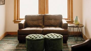 A cozy room with a brown leather sofa, two green ottomans, a small side table, and a unique light fixture.