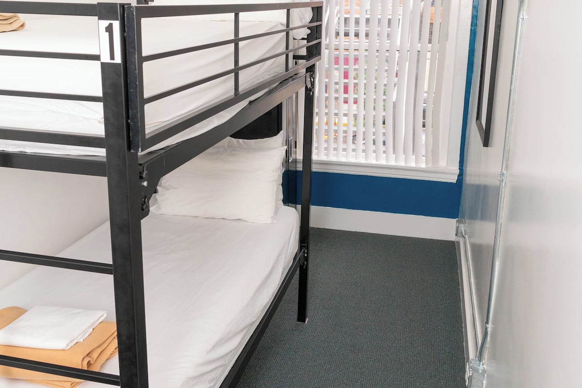 A bunk bed room with a blue accent wall, a window with blinds, and a refrigerator.