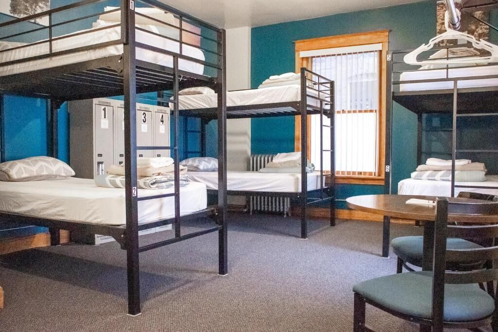 A dormitory room with bunk beds, a table, chairs, and lockers.