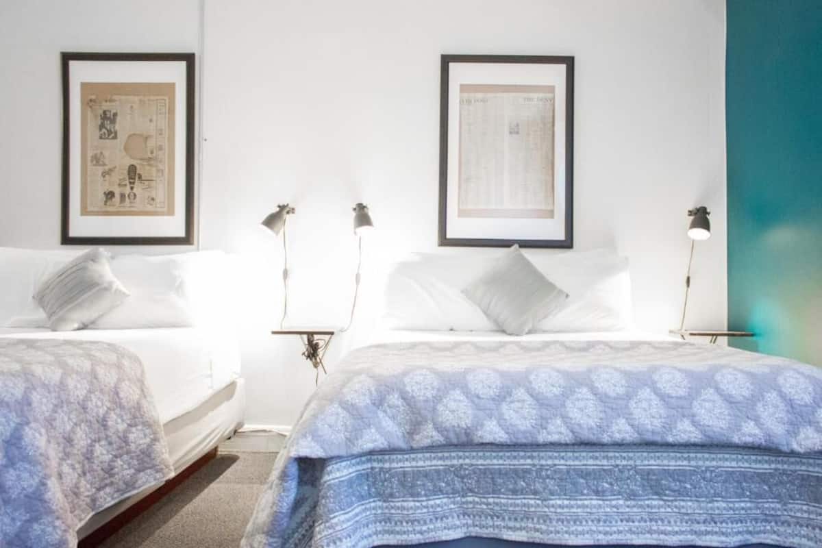 A hotel room with two beds, each with a headboard and bedside lamps. There are framed pictures on the wall above the beds.