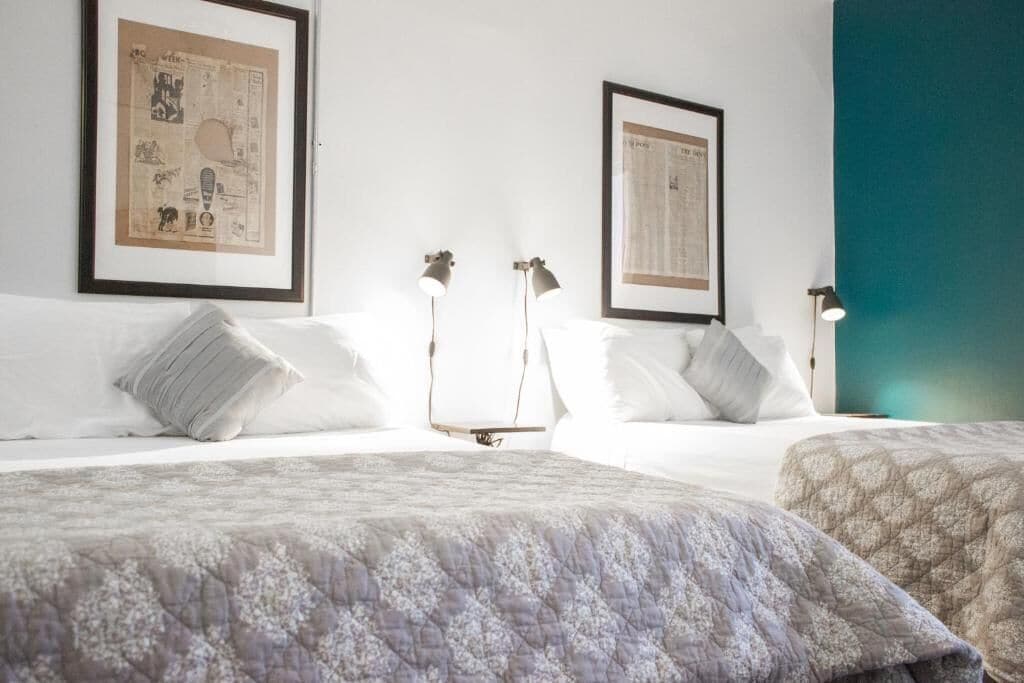 A hotel room with two beds, each with a quilted bedspread, two bedside lamps, and framed posters on the wall.