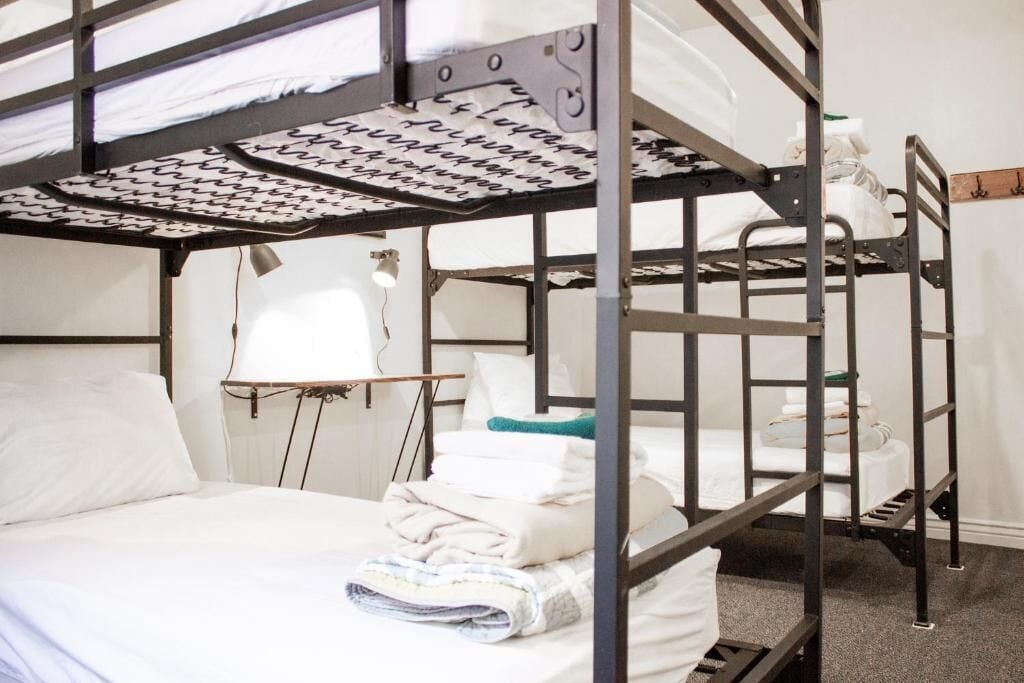 Habitación con literas, escritorio, silla, lámpara y ventana con cortinas blancas.