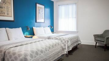 A hotel room with two beds, a chair, a window with blinds, and a framed picture on the wall.