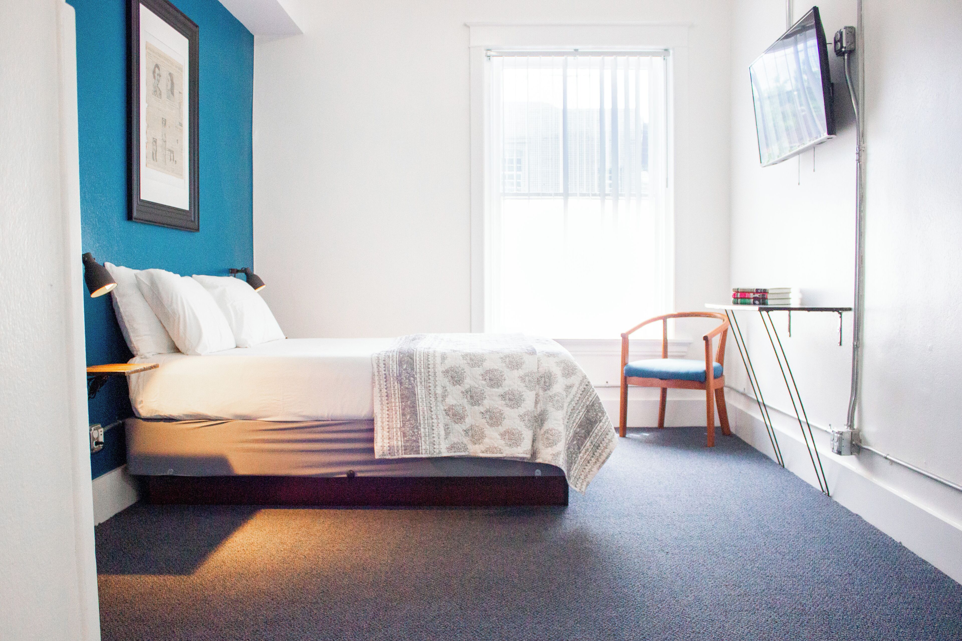 A bedroom with a bed, a chair, a TV, and a window.