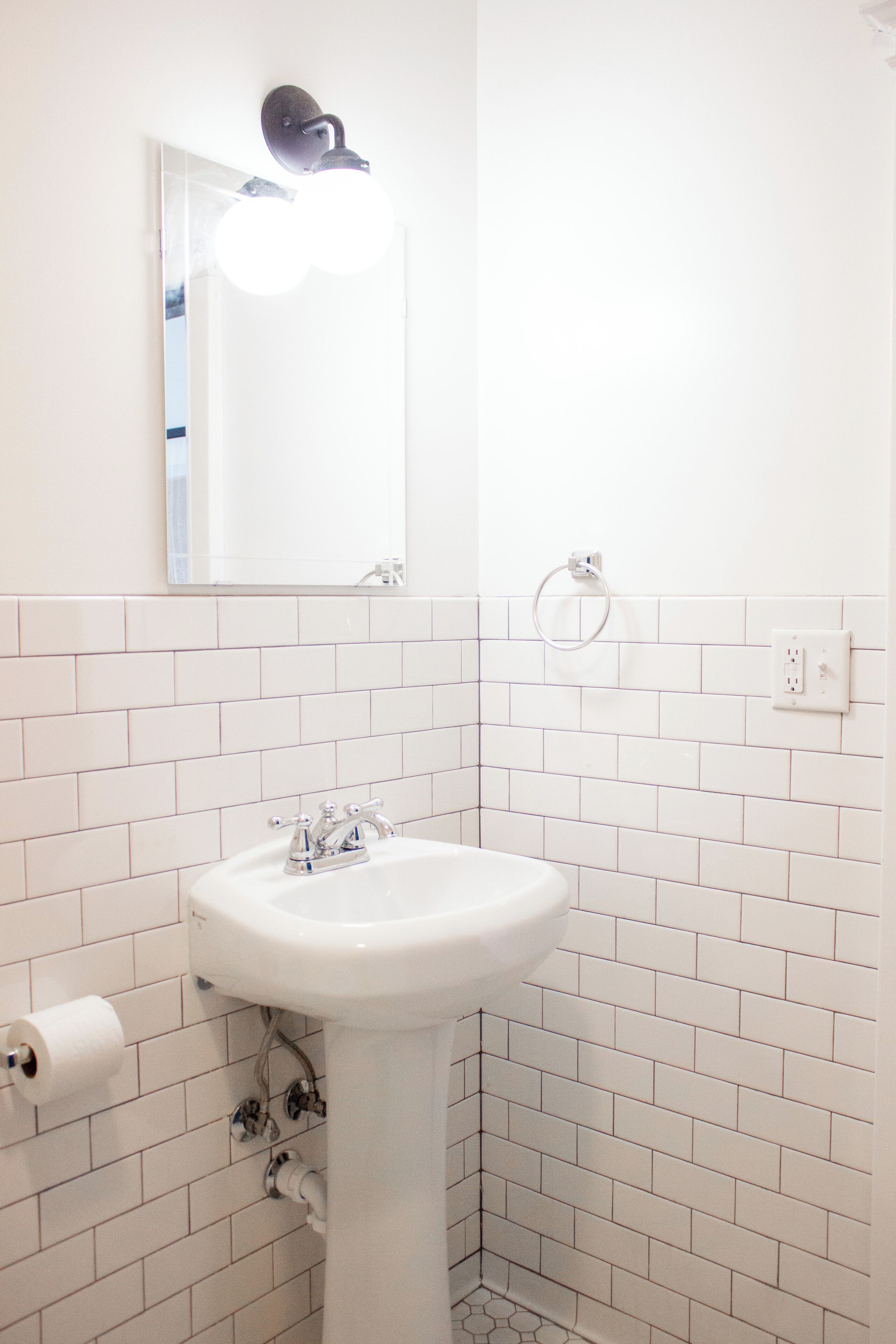 Un baño con lavamanos blanco, un espejo y un aro para toallas.