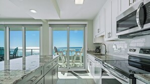 A modern kitchen with a view of the ocean, featuring a large window, a built-in microwave, and a granite countertop. - Gorgeous Upscale Remodel -LARGE 3 BEDROOM-Oceanfront Corner Condo - Dog Friendly (Orange Beach)