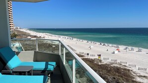 A balcony with blue chairs and a view of a beach with umbrellas and people. - Gorgeous Upscale Remodel -LARGE 3 BEDROOM-Oceanfront Corner Condo - Dog Friendly (Orange Beach)