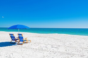 A beach with two blue lounge chairs and a blue umbrella.
