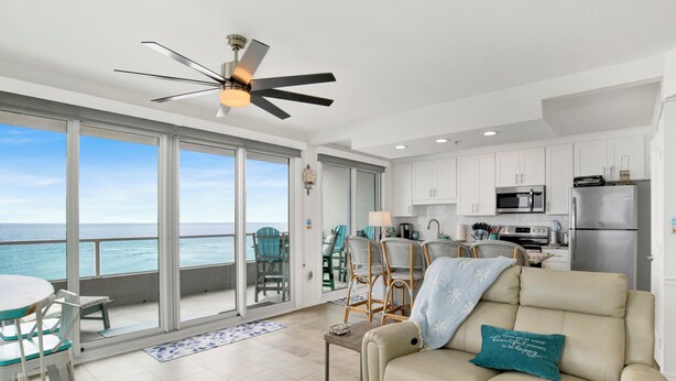 A modern living room with a sofa, a dining area with chairs, a kitchen with appliances, and a balcony with a view of the ocean. - Gorgeous Upscale Remodel -LARGE 3 BEDROOM-Oceanfront Corner Condo - Dog Friendly (Orange Beach)