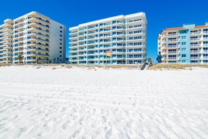 A beachfront hotel with multiple floors, balconies, and a sandy beach in the foreground.