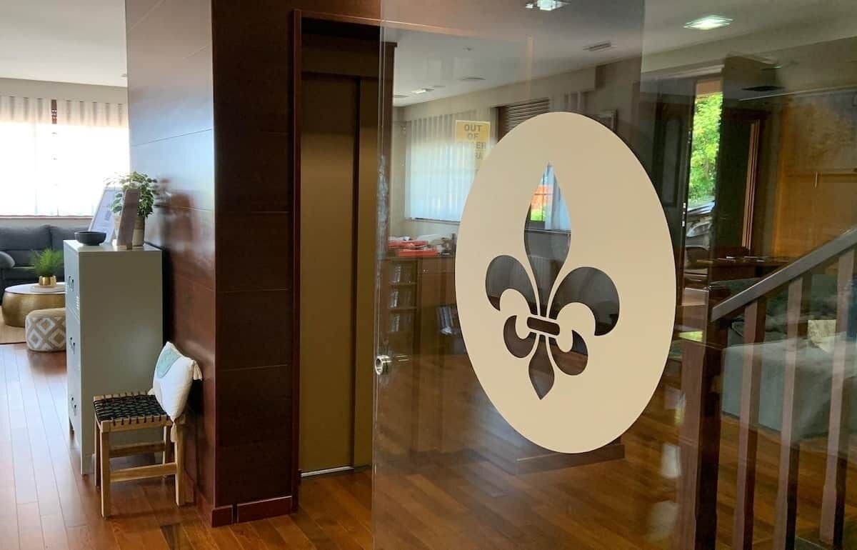Un interior moderno con suelo de madera, una puerta de cristal con un logotipo, una escalera y una zona de estar con cojines.