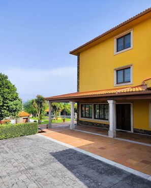 A yellow building with a tiled roof, a covered patio area, and a paved walkway. - Donato House (Narón)