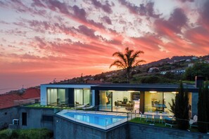 A modern house with a swimming pool, large glass windows, and a view of the surrounding landscape. - Luxury Villa Ocean View | Swimming Pool I Vincents Place (Estreito da Calheta)