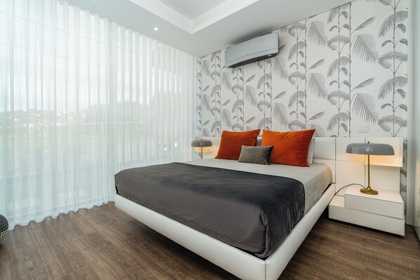 A modern hotel room with a large bed, a nightstand, a lamp, and sheer curtains. - Luxury Villa Ocean View | Swimming Pool I Vincents Place (Estreito da Calheta)