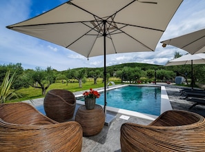 A poolside area with wicker furniture, umbrellas, and a view of a lush landscape. - Radiant and Secluded Villa With Pool (Rovinj)