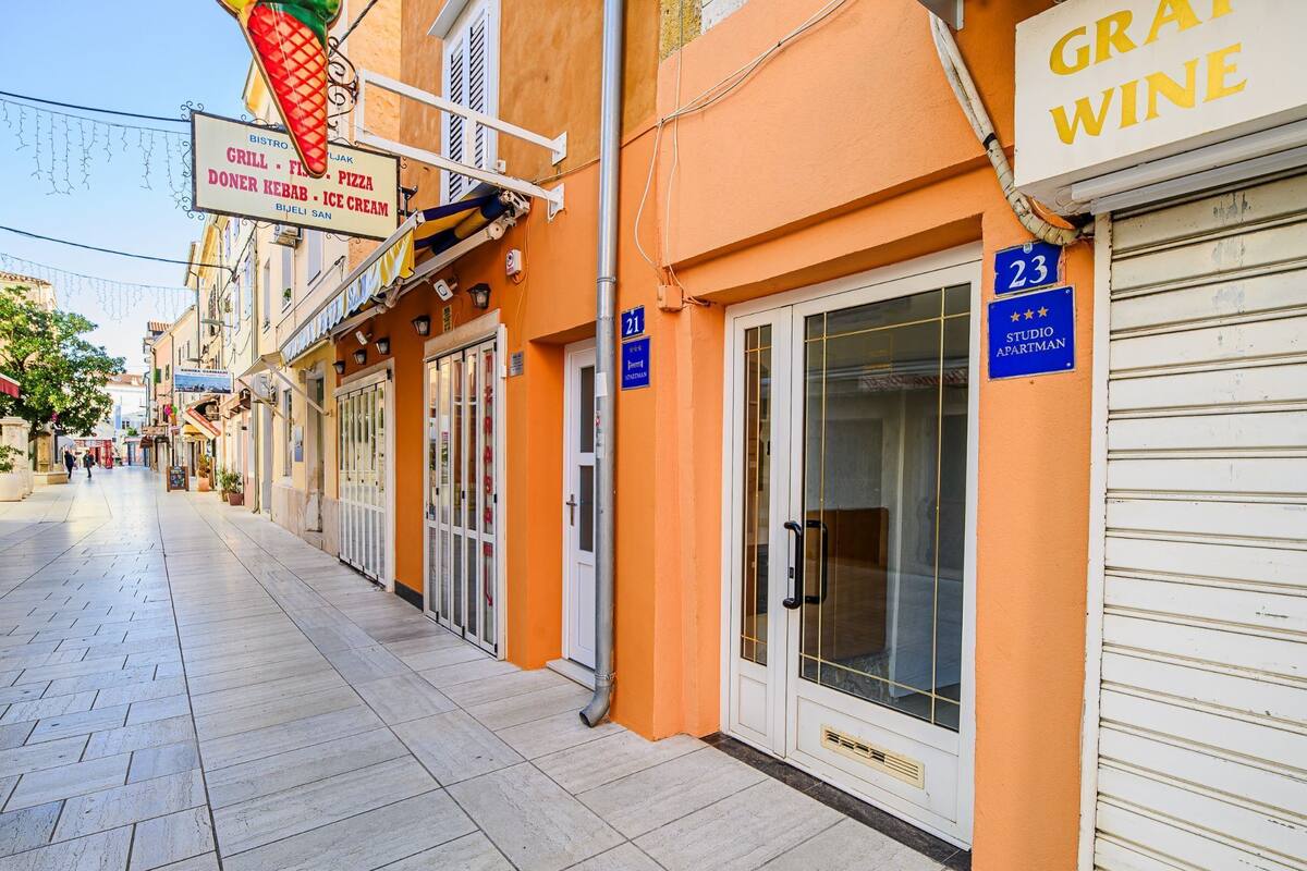 Eine Straße mit einer Reihe von Gebäuden, darunter ein Restaurant mit der Aufschrift 'BISTRO GRILL - PIZZA DONER KEBAB - ICE CREAM' und ein Weinkeller.