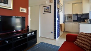 A compact living space with a TV, entertainment unit, and a red sofa. A kitchen area is visible with modern appliances and a tiled backsplash. - Comfortable and Sunny Rovinj Apartment (Rovinj)