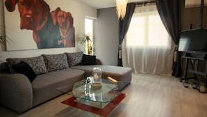 A living room with a sofa, a glass coffee table, a painting of dogs, a plant, and a television. - Scenic Rovinj Apartment With Balcony (Rovinj)
