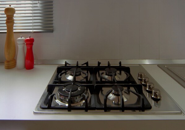 A kitchen with a gas stove, two salt and pepper shakers, and a window with blinds. - Scenic Rovinj Apartment With Balcony (Rovinj)